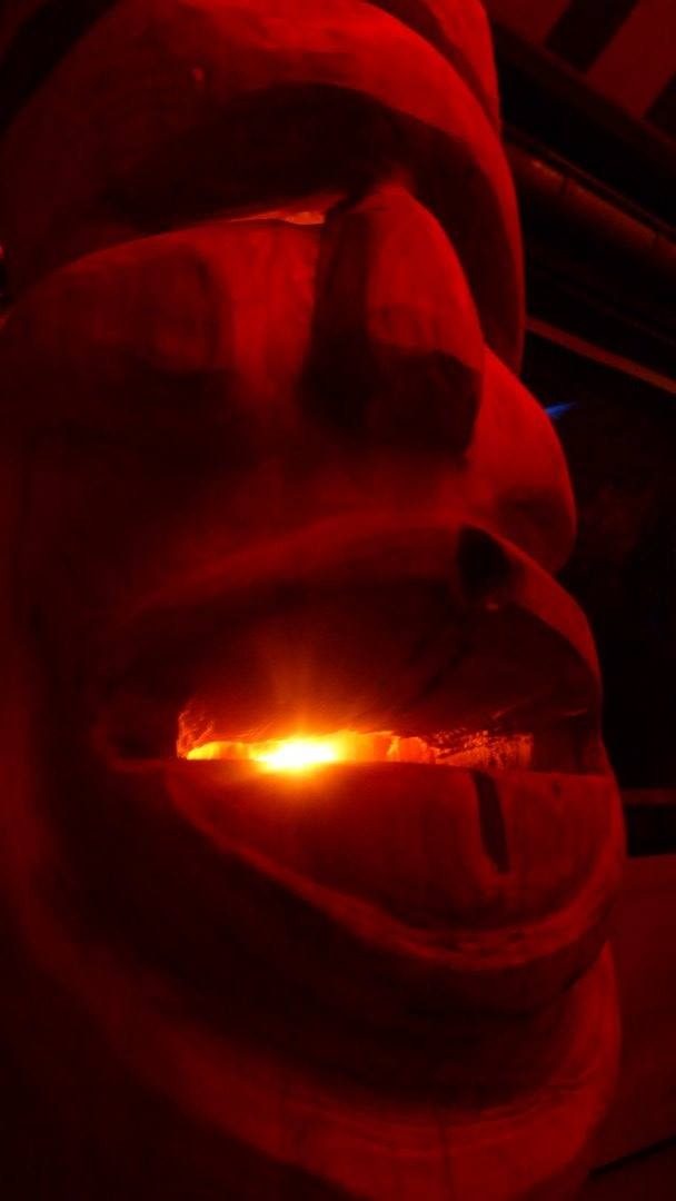 Grand visage sculpté éclairé en rouge, une lumière brille entre ses lèvres.